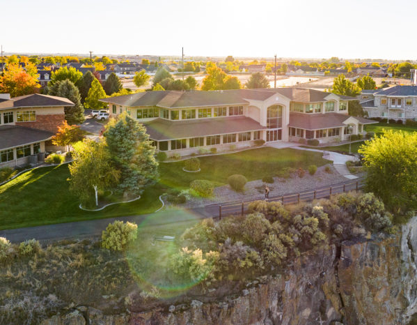 Aerial shot of Twin Falls, Idaho office. Its a large building that looks like a residential living space with a lot of windows. The building appears to be sitting alongside a rock cliff.